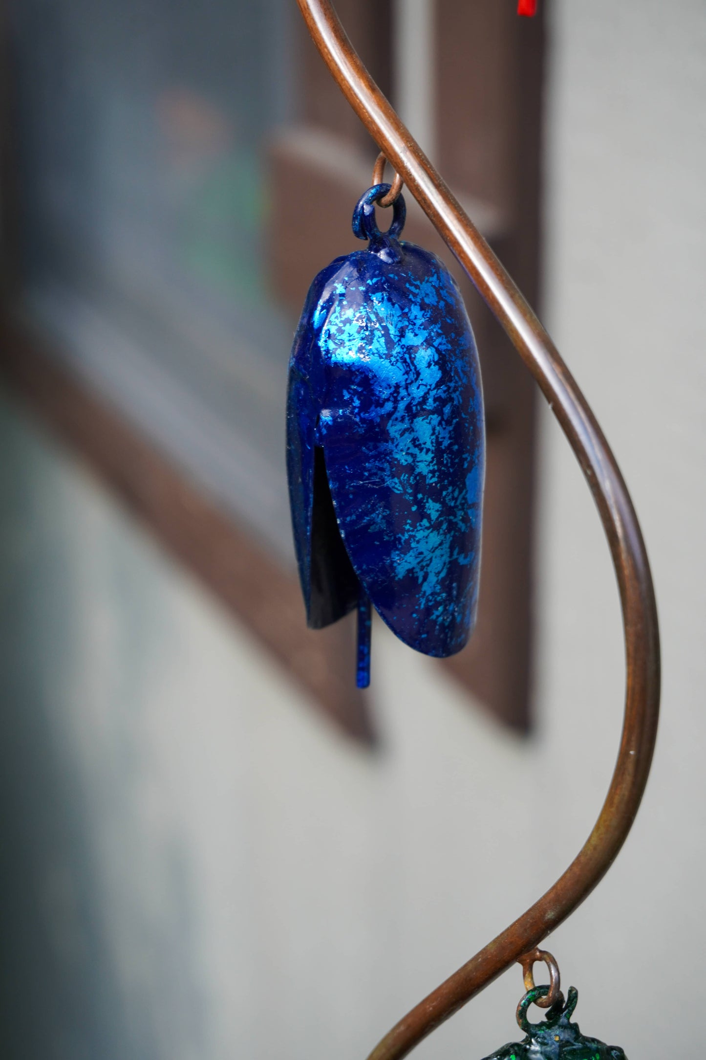 A glossy, metallic blue leaf-shaped hanging ornament with a marbled texture, suspended from a curved copper-colored metal rod.