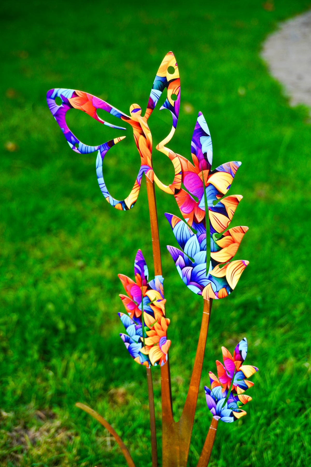 Colorful butterfly and tropical flower garden stakes with a vibrant multicolor pattern, set against a blurred green grass background.