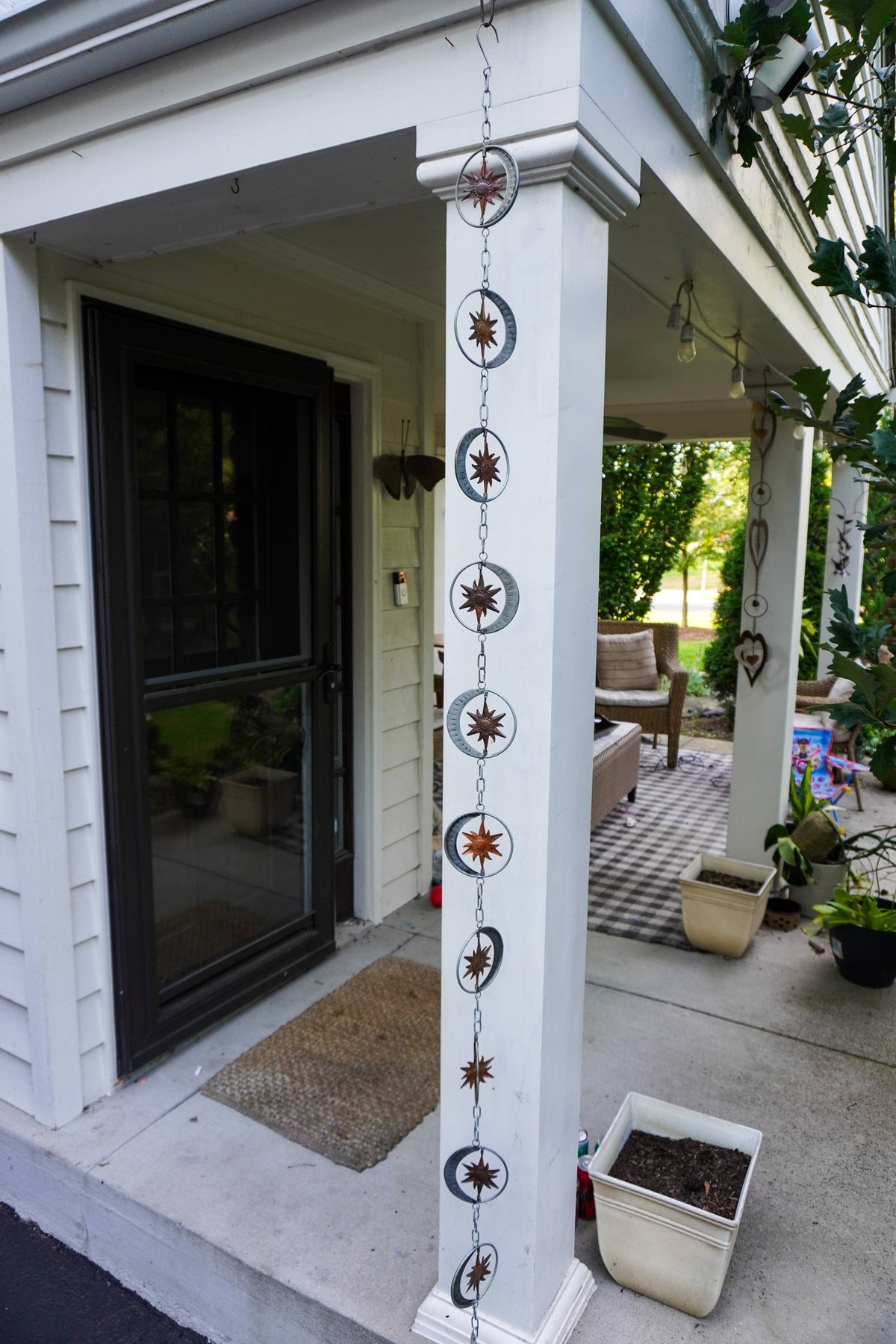 A decorative hanging chain with sun and moon metal medallions and starburst motifs displayed on a white porch column in front of a house entryway.