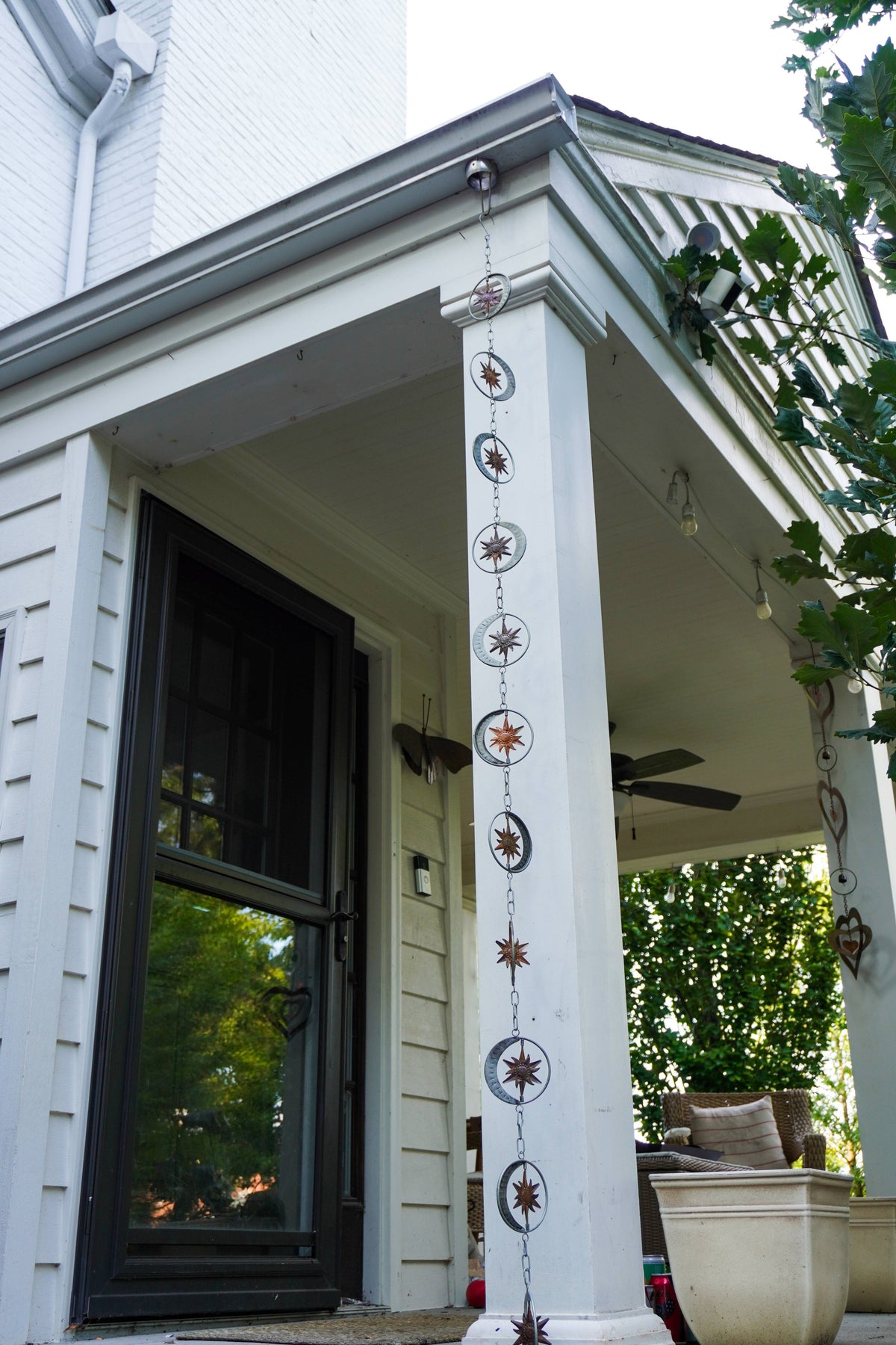 A decorative hanging chain with circular medallions and starburst motifs displayed vertically on a white porch column of a house.
