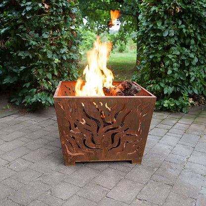 Corten steel fire pit with flames burning on a paved patio surrounded by greenery.