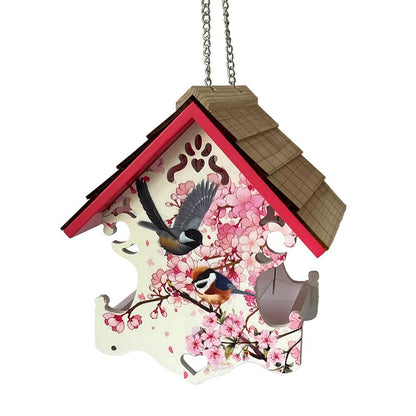 A hanging birdhouse-shaped decorative feeder with a pink cherry blossom print, two birds, and a brown shingled roof, shown on a plain white background.
