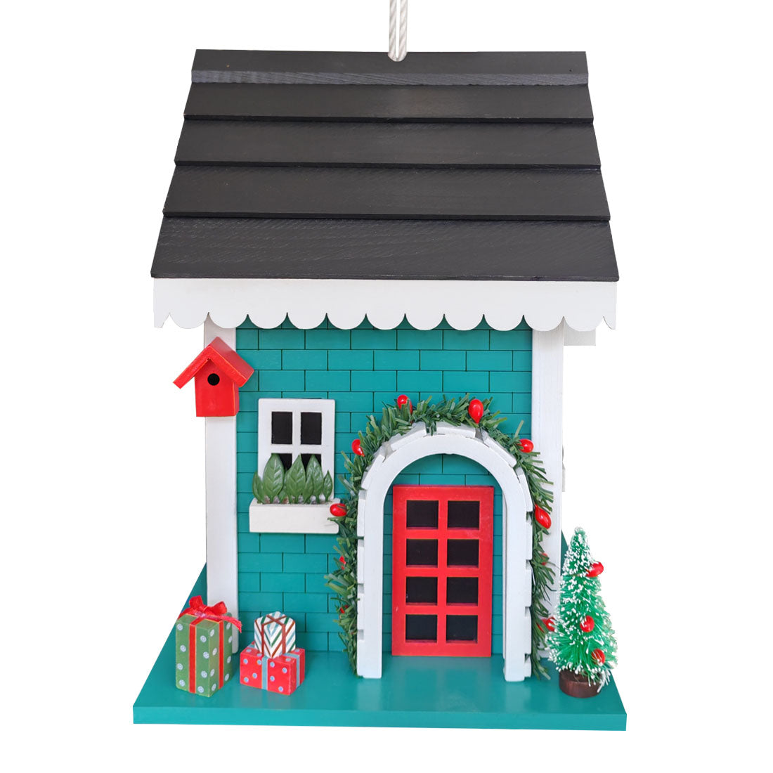 A decorative Christmas bird house featuring a teal brick facade, a dark gray roof, a red door, white trim, green garland with red berries, a small tree, and holiday gifts, shown on a plain white background.