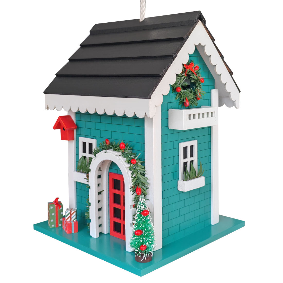 A decorative Christmas bird house shaped like a teal and white cottage with a dark gray roof, red door and chimney, green wreaths, a small Christmas tree, and wrapped gifts on a white background.
