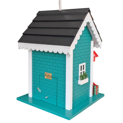 A decorative birdhouse shaped like a small house with turquoise walls, a black shingled roof, white trim, a small window with a plant, and a red flag, shown on a plain white background.