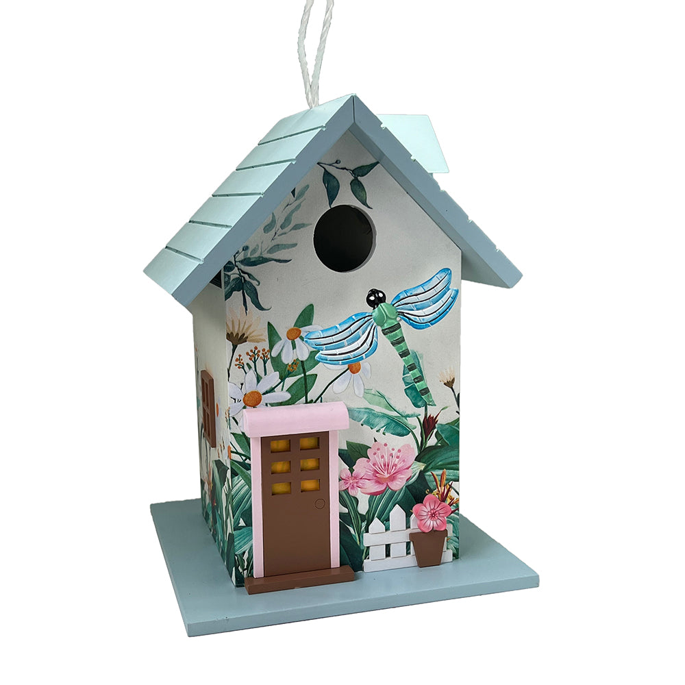 A decorative birdhouse shaped like a cottage with a light blue roof and base, decorated with tropical floral and dragonfly illustrations. It features a brown door with yellow window panes, a pink trim, and a white hanging string at the top, shown against a plain white background.