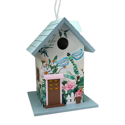 A decorative birdhouse shaped like a cottage with a light blue roof and base, decorated with tropical floral and dragonfly illustrations. It features a brown door with yellow window panes, a pink trim, and a white hanging string at the top, shown against a plain white background.