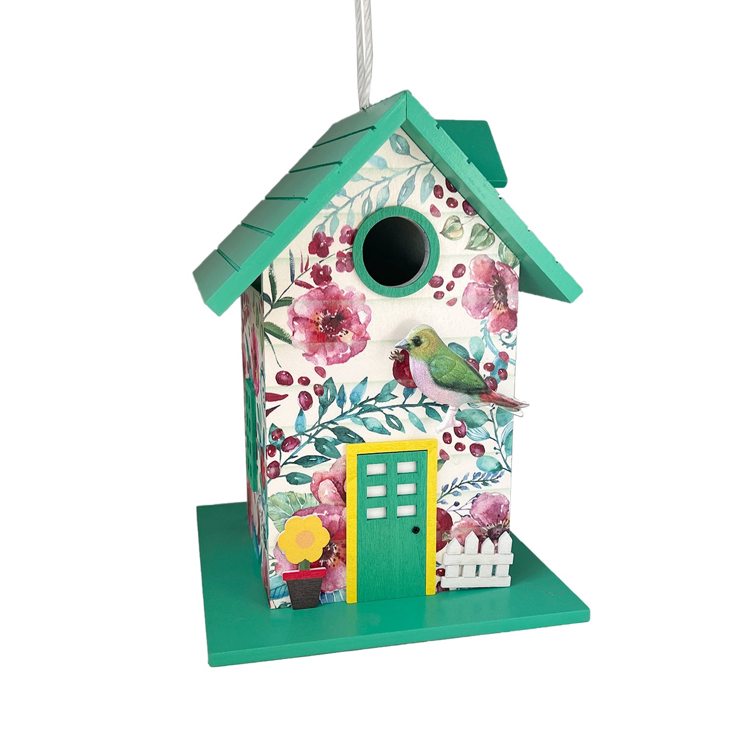 A decorative birdhouse with a teal green base and roof, covered in a floral print with pink flowers and green leaves. It features a small yellow door, a miniature white picket fence, a potted plant, and a small green bird figurine perched on the side.