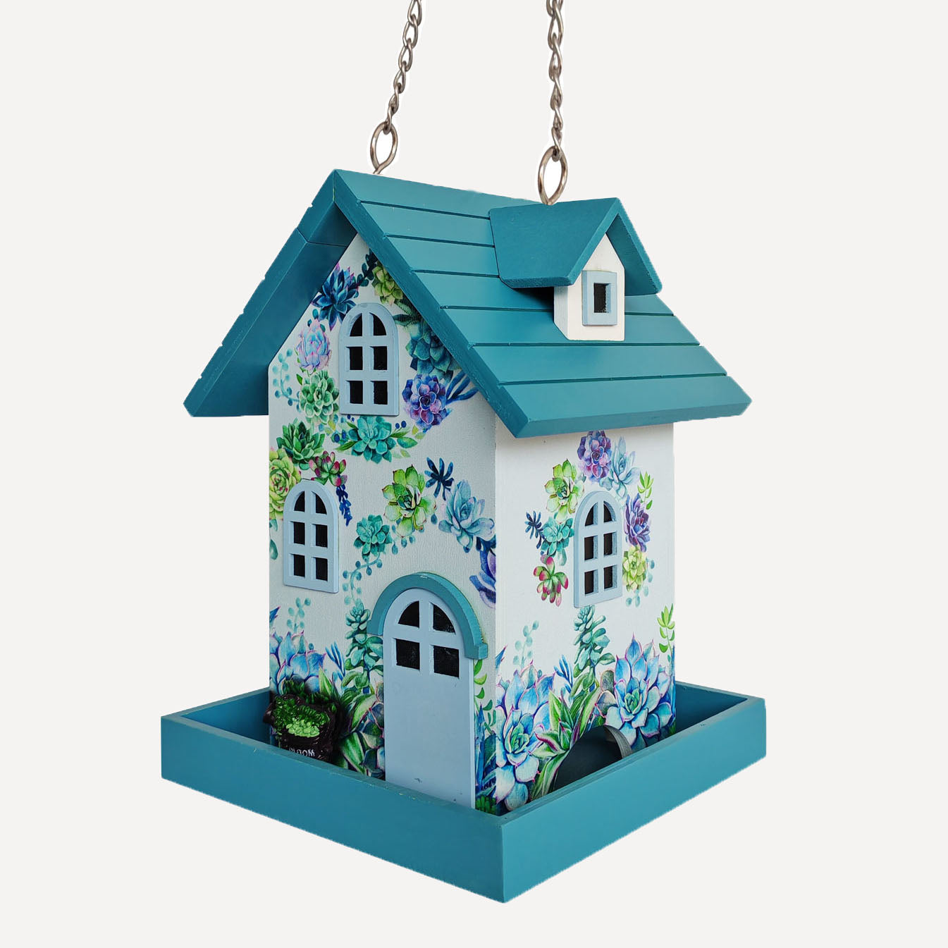 A hanging bird feeder with a teal roof and tray, decorated with a white front and sides covered in colorful floral and butterfly illustrations, suspended by metal chains against a light gray background.