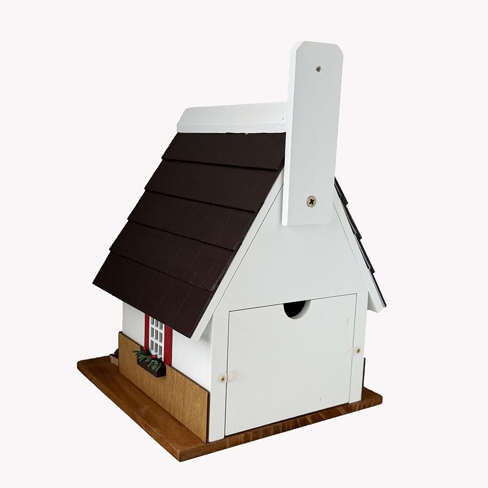 A small house-shaped birdhouse with a dark brown shingled roof, white body, brown base, and a small red window detail, photographed on a plain light background.