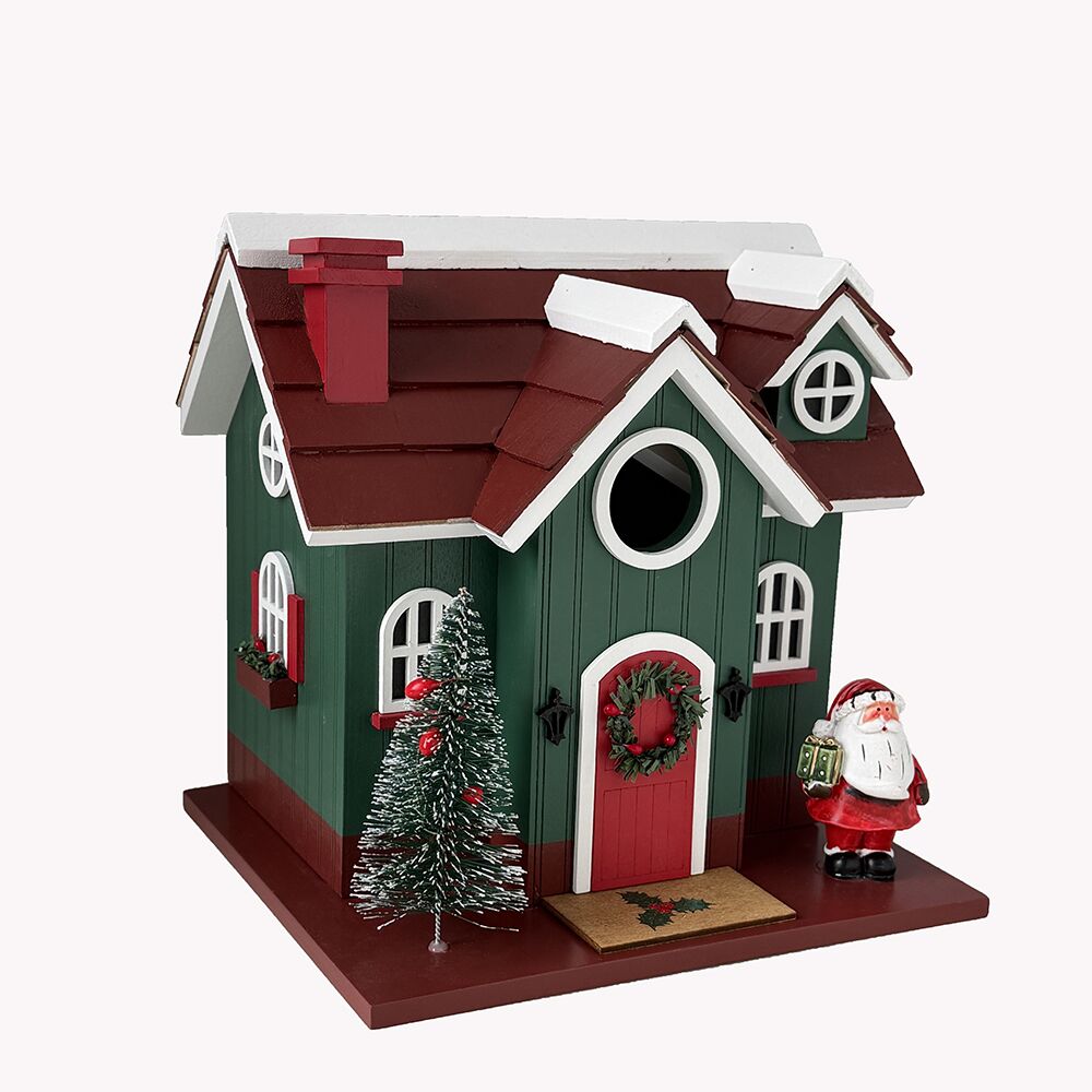 A decorative Christmas birdhouse with a dark green body, dark red roof and door, white trim, a small Christmas tree, and a Santa Claus figure beside it, shown on a plain light background.