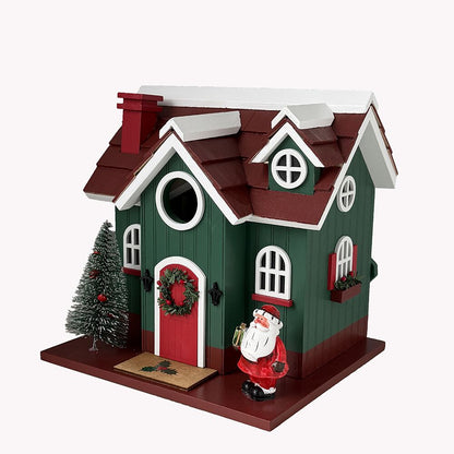 A decorative Christmas birdhouse with a green body, dark red roof, white trim, a red front door with a wreath, a small Christmas tree, and a Santa Claus figure standing on the front base.