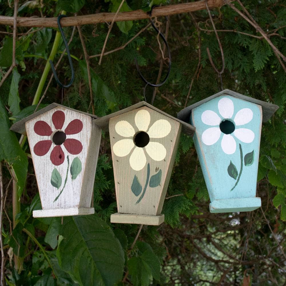 Three hand-painted wooden birdhouses hanging from a tree branch outdoors, decorated with floral designs in red, cream, and light blue.