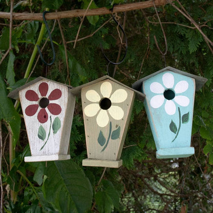 Three hand-painted wooden birdhouses hanging from a tree branch outdoors, decorated with floral designs in red, cream, and light blue.