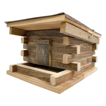 A rustic wooden beehive box made from stacked natural wood planks, featuring a slanted lid with a metal wire hook and a bottom entrance frame, shown on a plain white background.