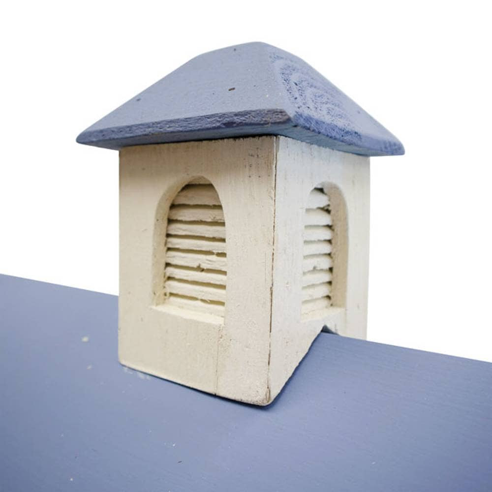 A small hand-painted wooden birdhouse with a distressed cream-colored body and a slate blue-gray roof, shown on a blue surface against a white background.