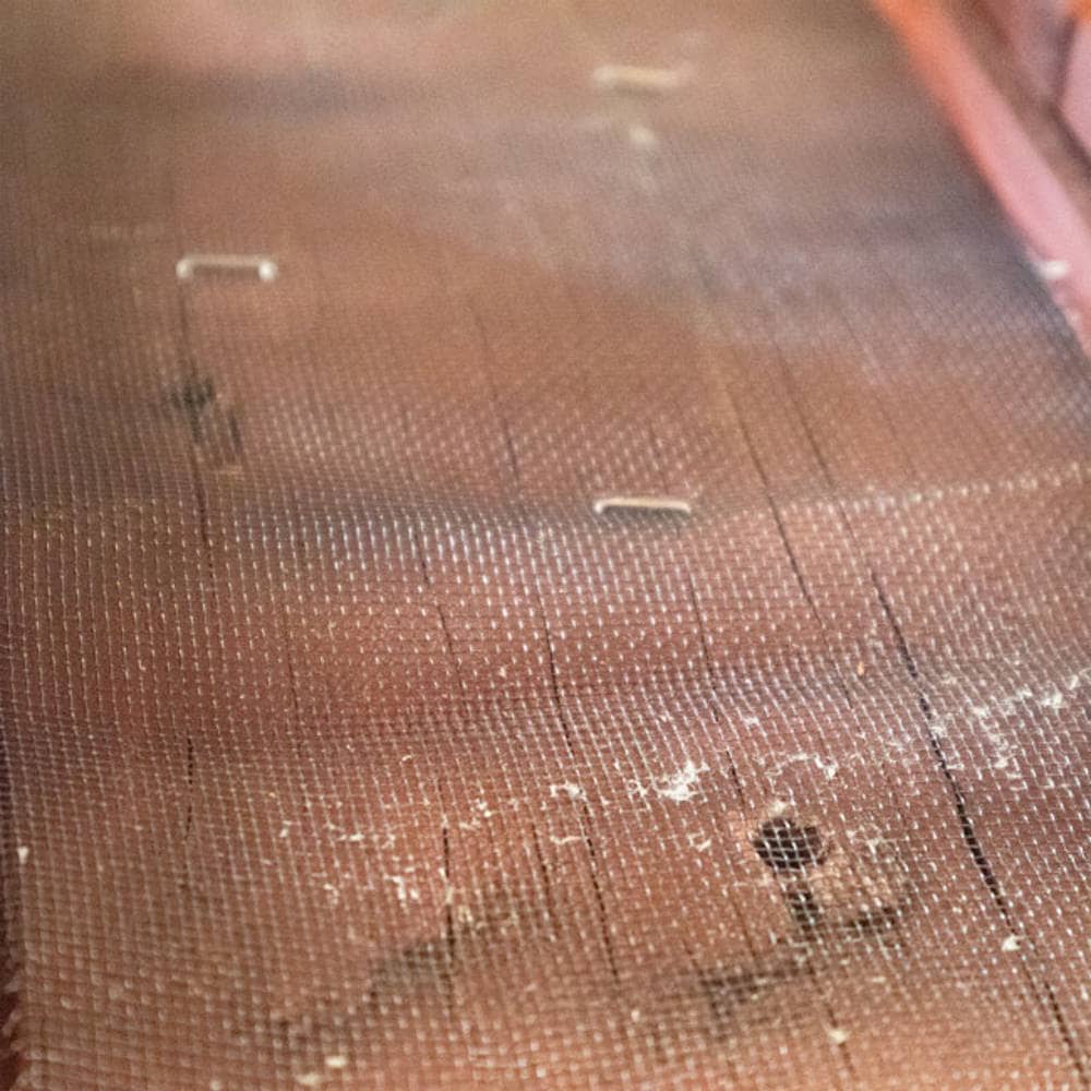 A close-up view of a brown mesh screen or filter material with a fine woven texture, laid over a wooden surface.