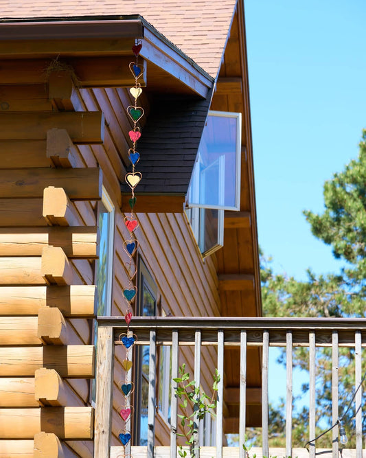 Hanging chain of multicolor stained glass hearts in metal frames, suspended from a rooftop eave outdoors