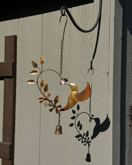 Rusty metal hummingbird wind chime with heart-shaped leaf branch and small bell, hanging outdoors in autumn