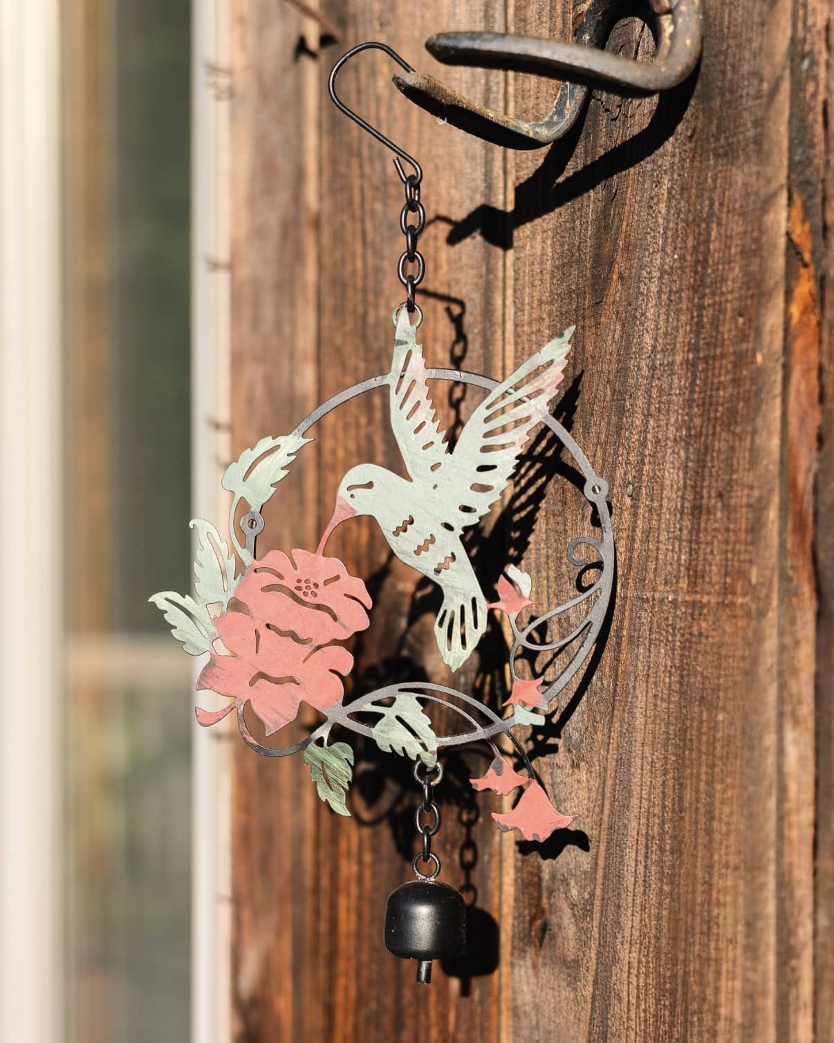 Metal wind chime ornament featuring a hummingbird and pink flowers with a hanging black bell, in mint green and pink tones