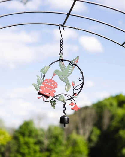 Metal circular garden ornament with green hummingbird, red rose, and trumpet flowers, hanging with a small black bell
