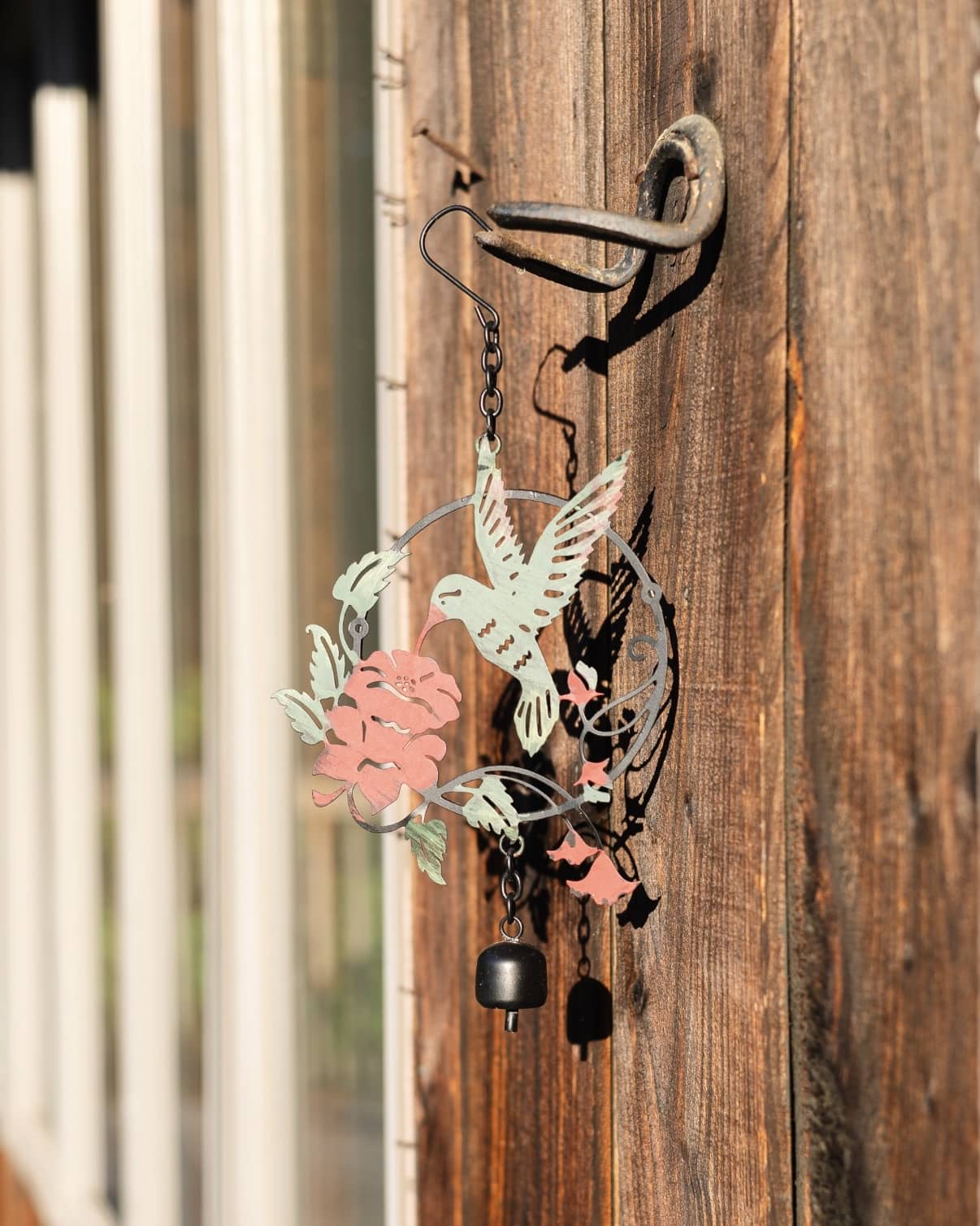 Metal wind chime ornament featuring a hummingbird and pink flowers in mint and coral tones with a small black bell