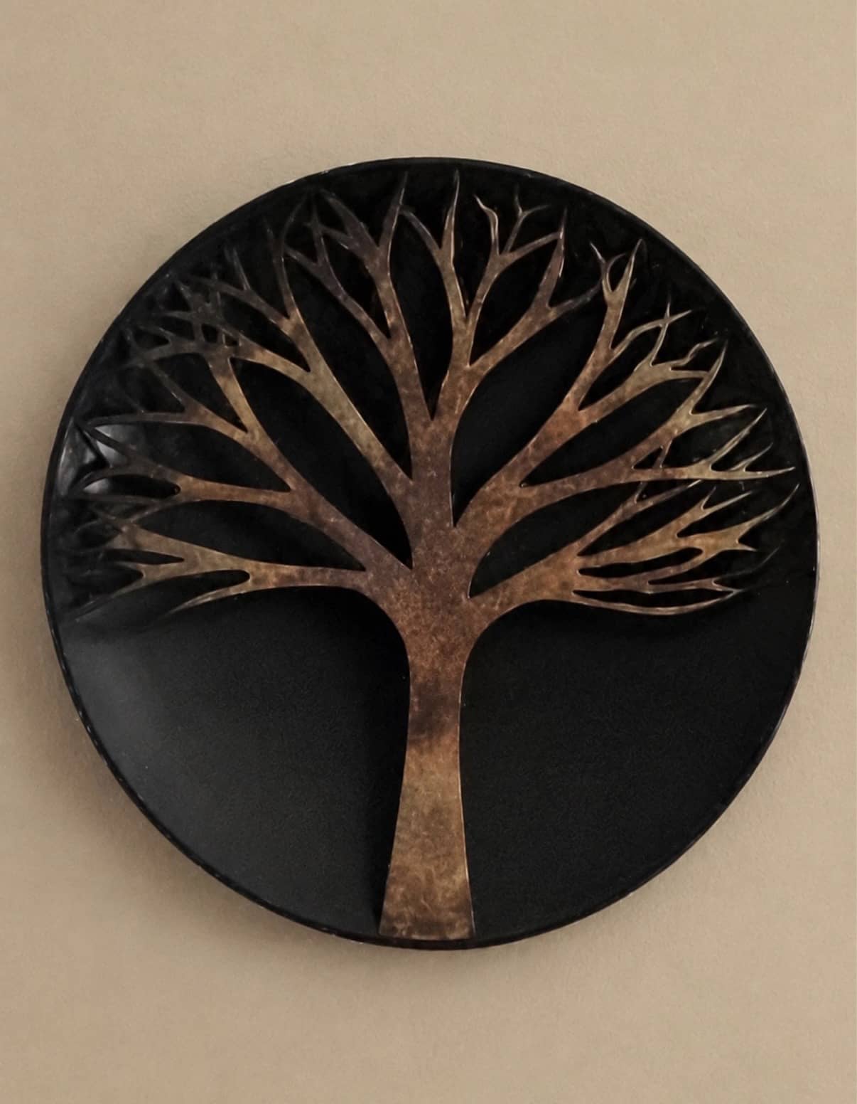 Round black metal wall disc with a raised copper-toned bare tree silhouette branching across the upper half