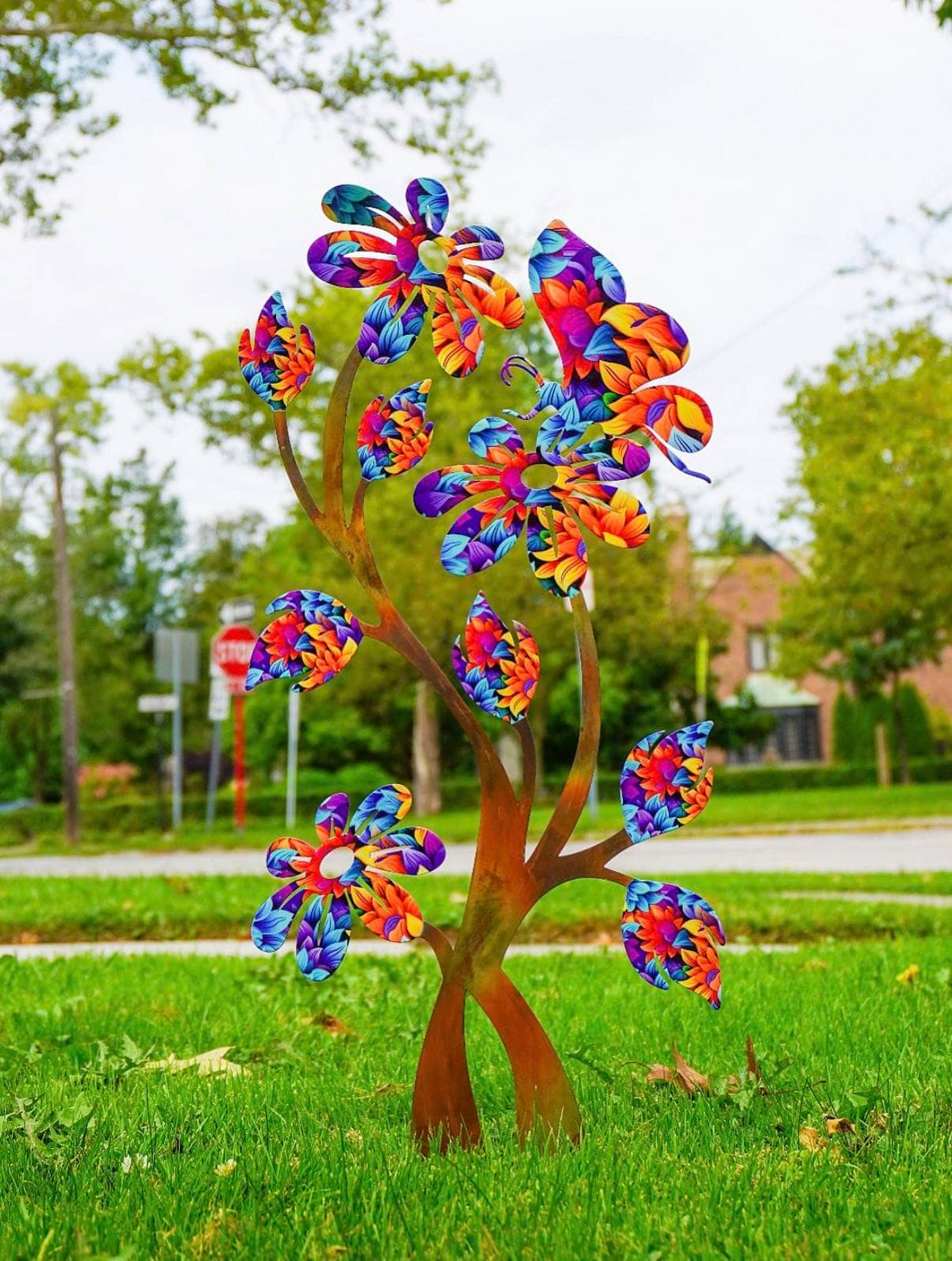 A colorful metal flower sculpture shaped like a tree, standing on a green lawn in an outdoor residential setting.