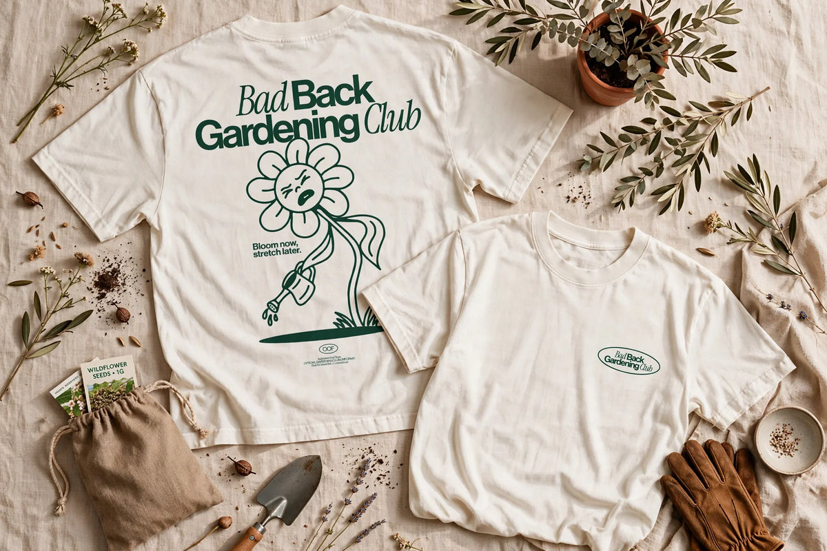 Two off-white graphic t-shirts displayed in a styled flat-lay with gardening props. The larger shirt shows the back with the text 'Bad Back Gardening Club' and a flower illustration, while the smaller shirt shows the front with a small matching logo on the chest.