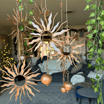 Three copper metal sun-shaped hanging mobiles with flame rays, mirrored centres, and dangling ball bells
