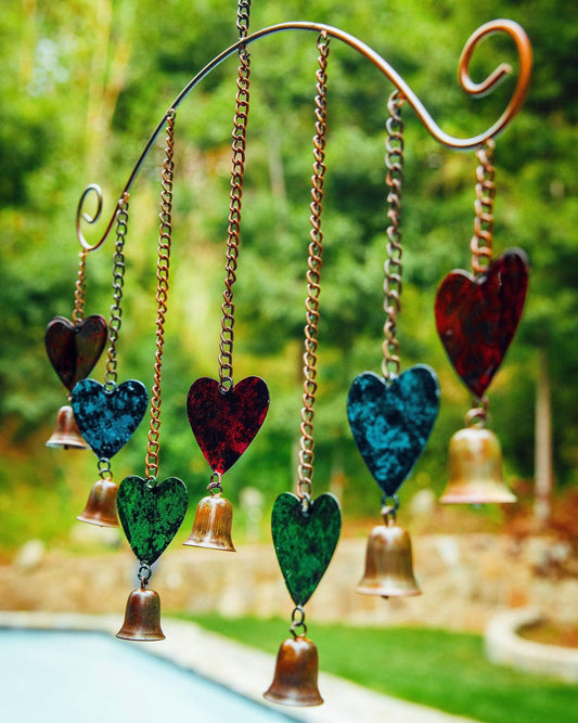 Copper wind chime with red, teal, and green metal hearts and brass bells hanging from chains on a curved bracket