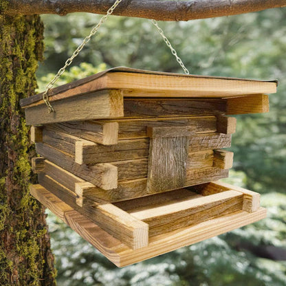 A rustic wooden bird feeder hanging from a metal chain attached to a tree branch outdoors, with blurred green foliage in the background.