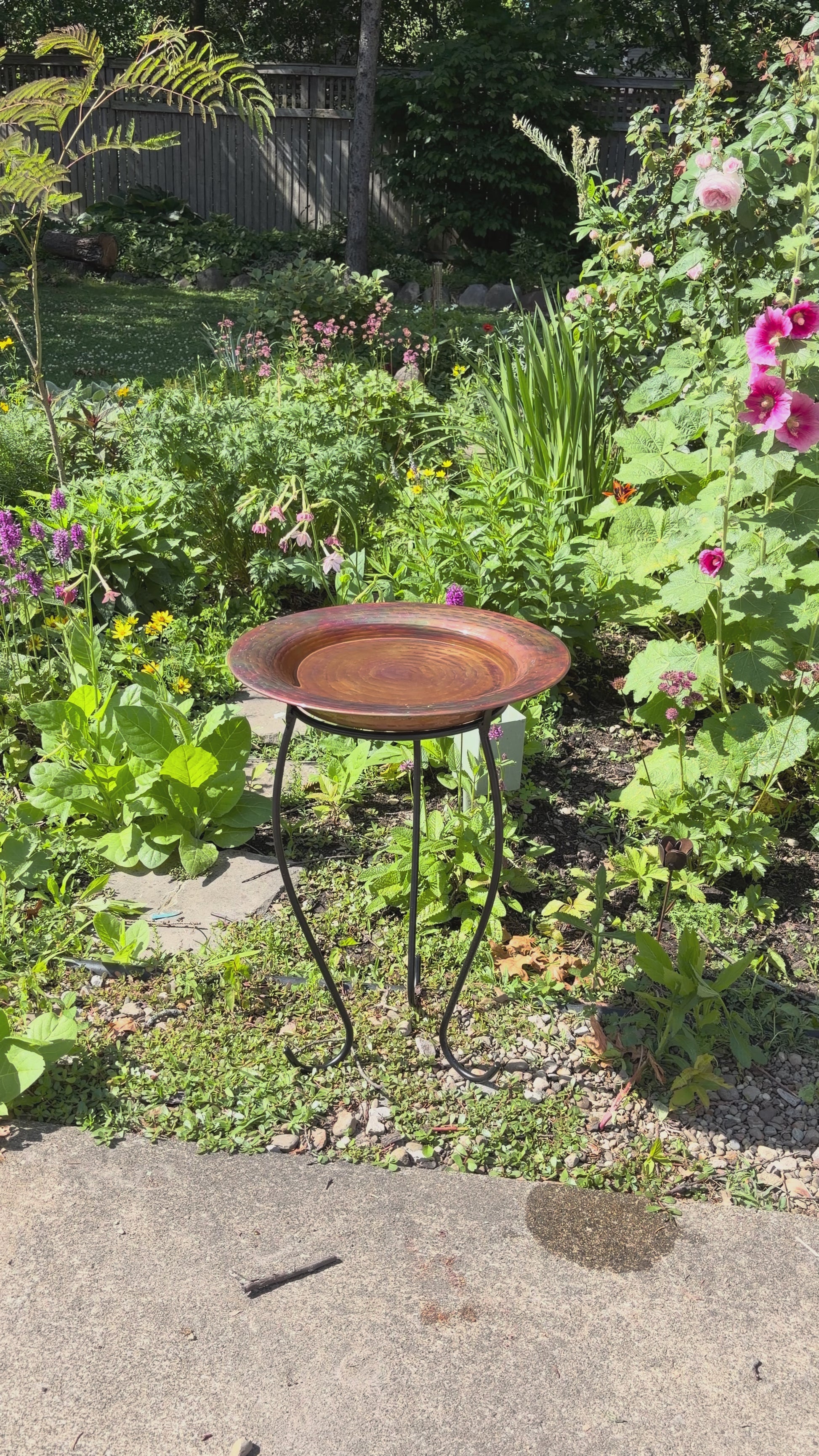 Hammered copper round birdbath with iridescent finish on curved metal stand.