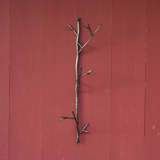 Bronze-toned metal twig-shaped wall hook with branching arms mounted on a red wooden panel